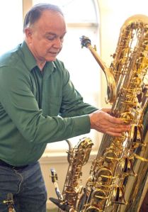 Tim Price picks up his bass saxophone while talking about his collection. Dean Hare/Daily News